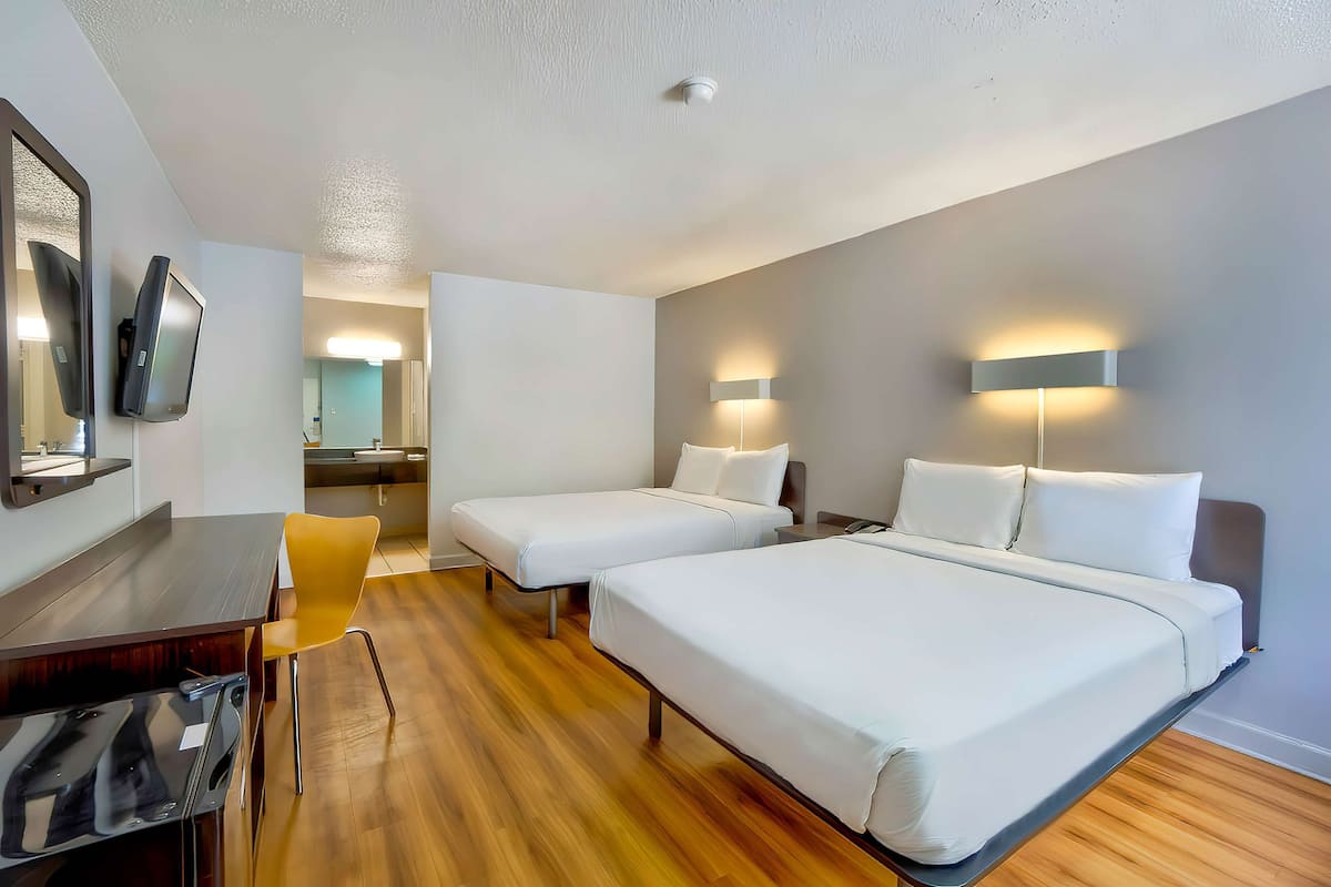 A hotel room with two beds, a desk, a chair, and a television.