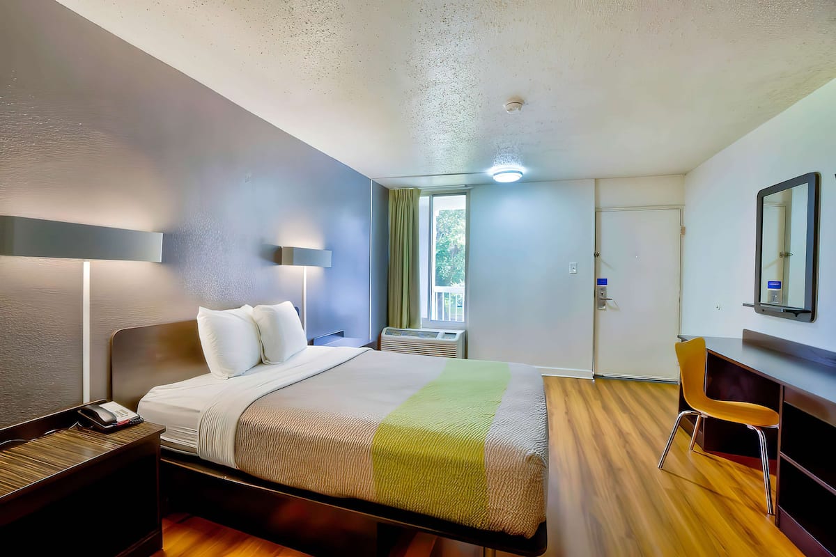 A hotel room with a bed, bedside table, lamp, chair, and a desk.