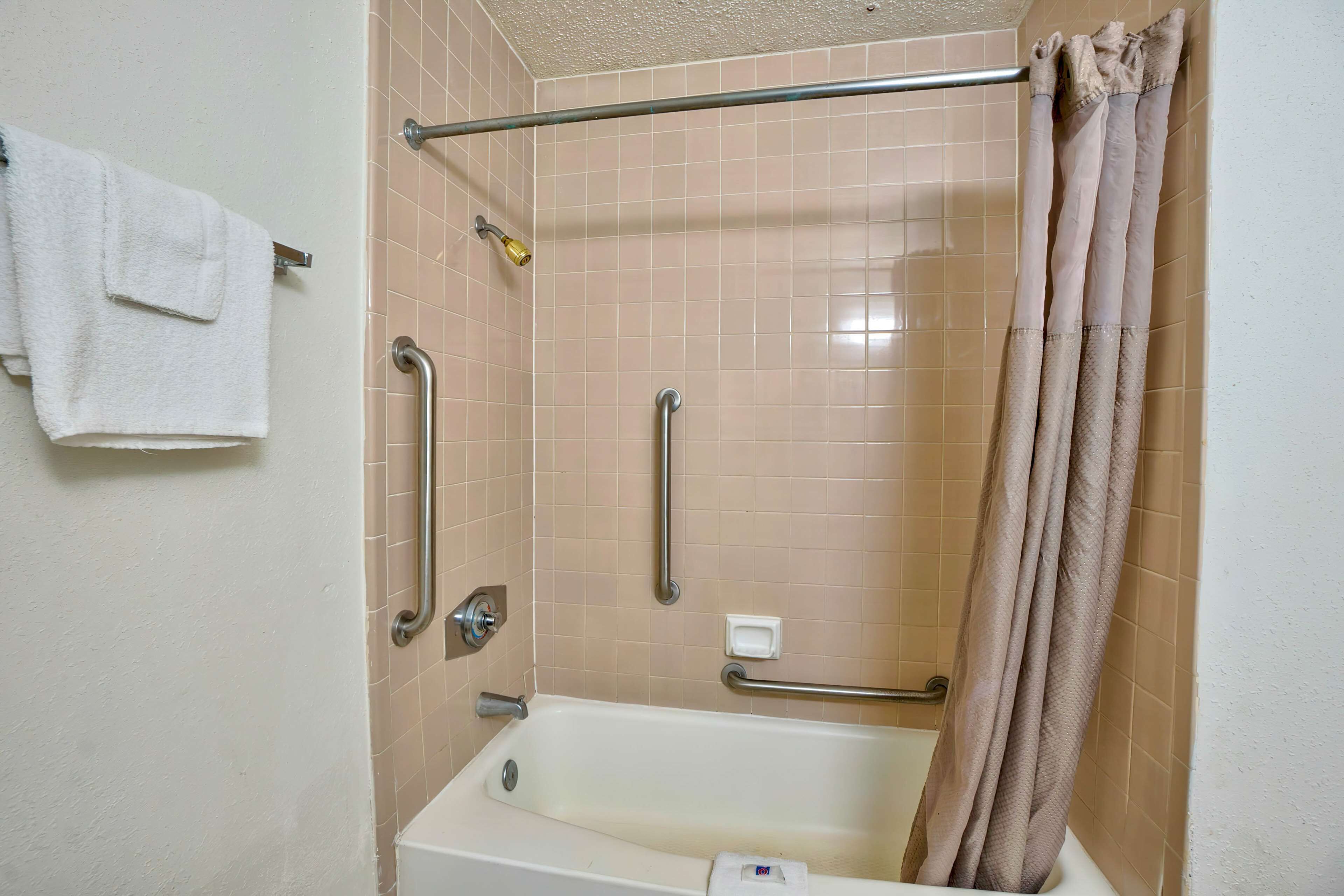 A bathroom with a bathtub, grab bars, a shower curtain, and a towel rack.