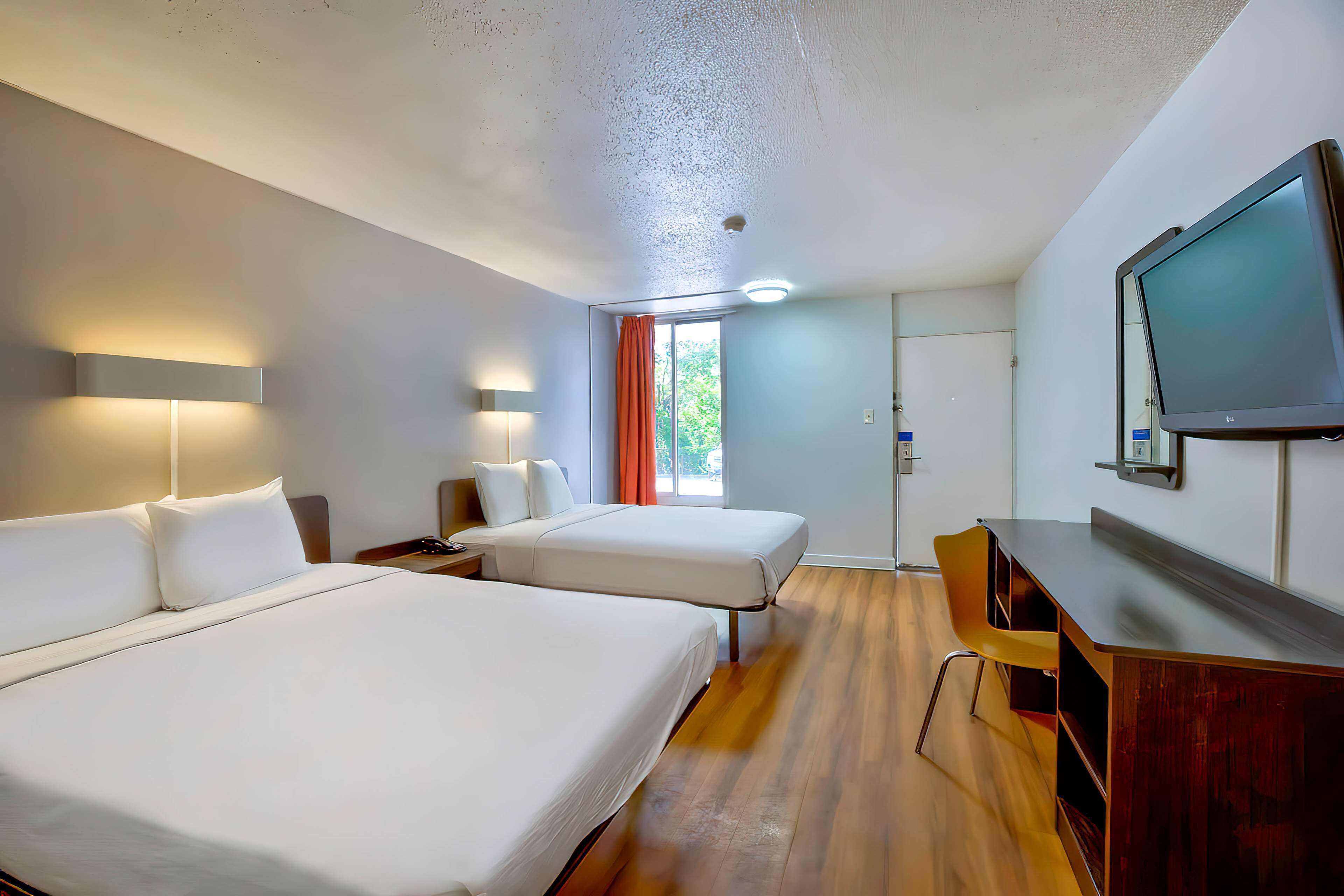 Une chambre d’hôtel avec deux lits, un bureau, une télévision et une fenêtre avec des rideaux.
