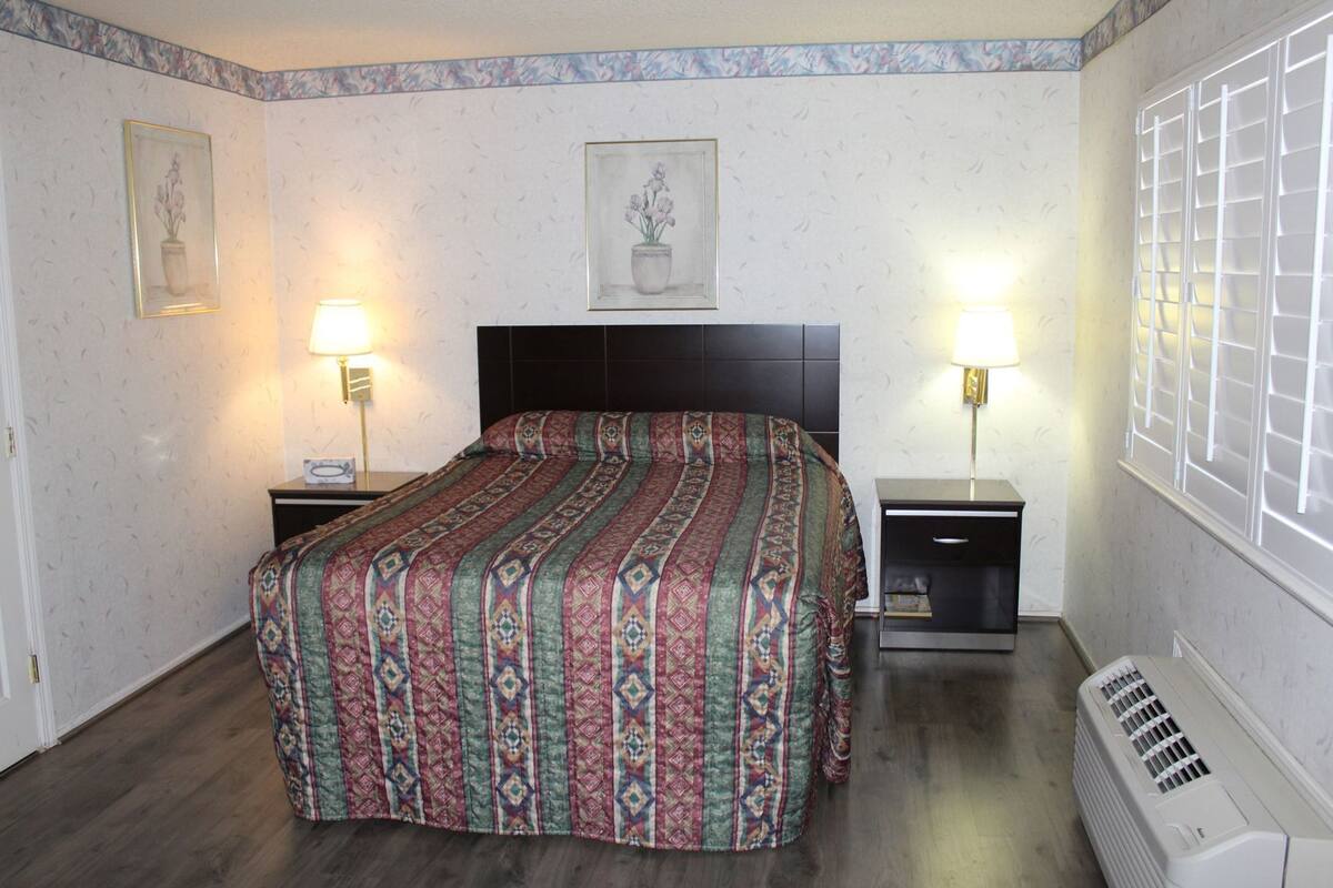 A bedroom with a bed, two bedside tables with lamps, a heater, and two framed pictures on the walls.