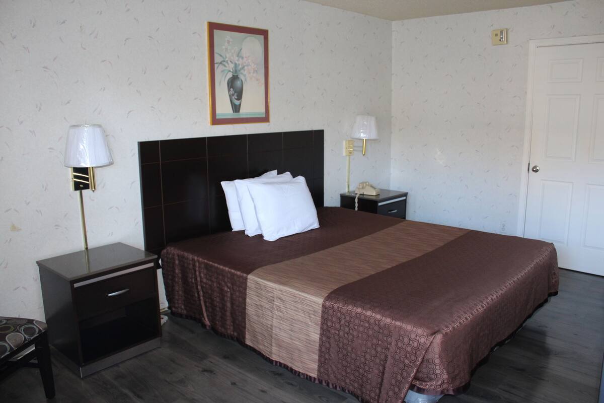 A hotel room with a large bed, two bedside tables, a nightstand, a lamp, a telephone, and a door.
