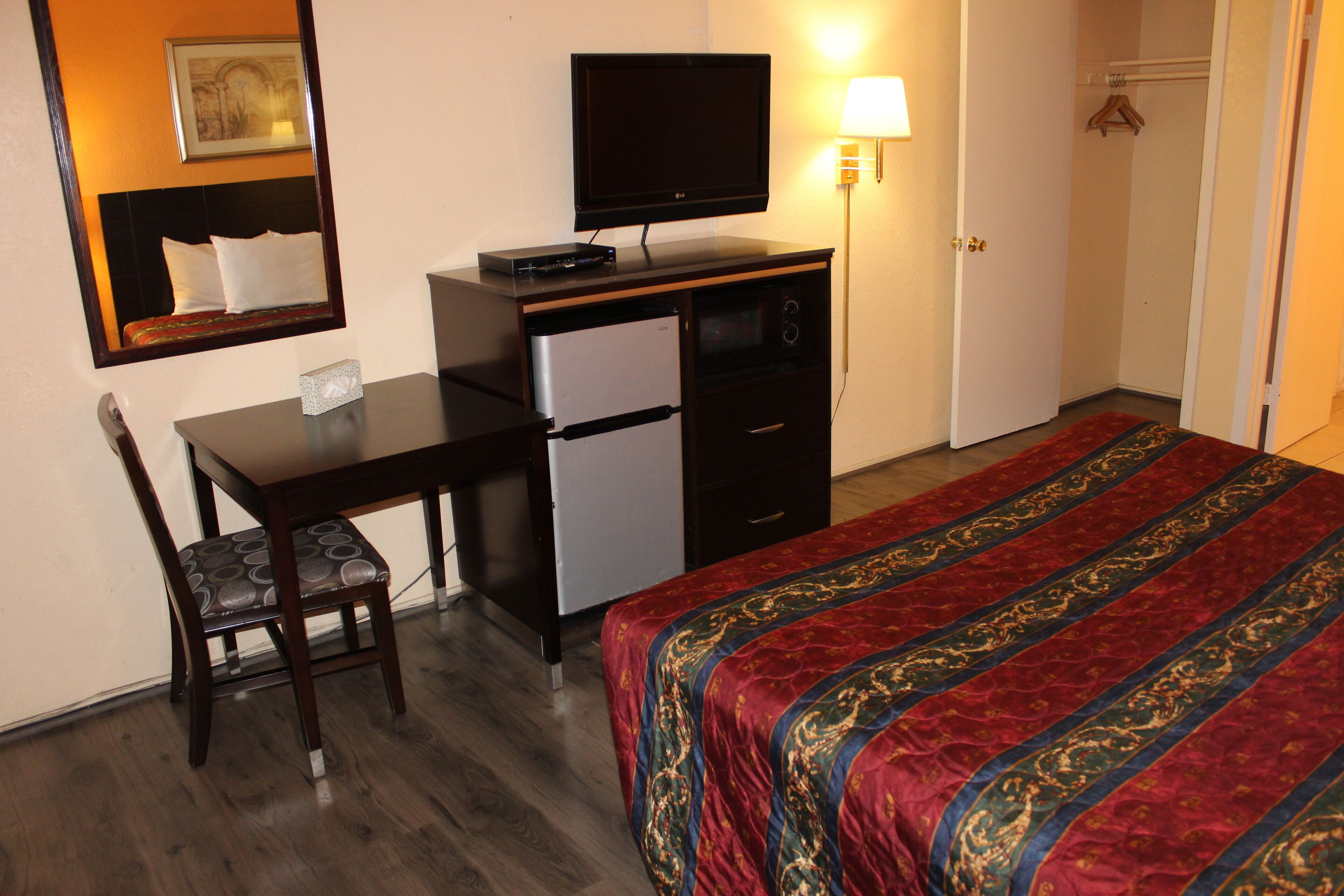 Ein Hotelzimmer mit einem Bett, einem Schreibtisch mit Fernseher, einem Kühlschrank, einem Sessel und einer Lampe.