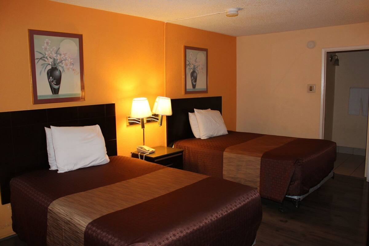 A hotel room with two beds, a nightstand with lamps, and two framed floral paintings on the wall.