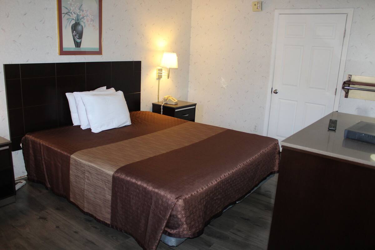 A hotel room with a neatly made bed, a bedside lamp, a telephone, and a door.