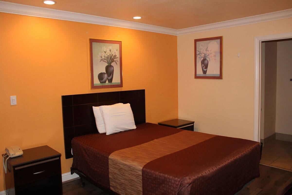 A hotel room with a bed, bedside tables, a phone, and two framed pictures on the walls.