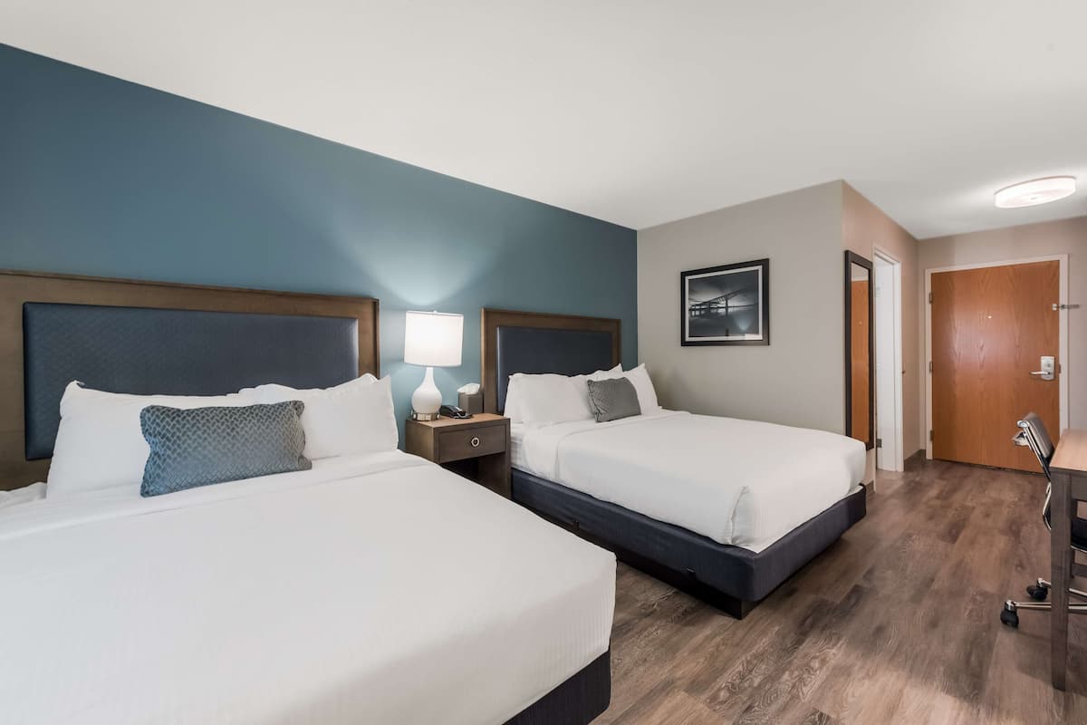 A hotel room with two beds, wooden headboards, a desk, and a chair.