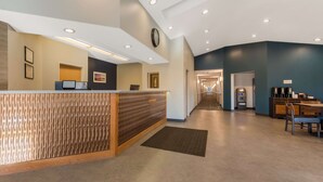 Zona de recepción de hotel con un mostrador de madera, un reloj en la pared y una máquina de café al fondo.