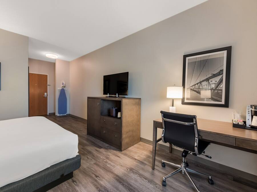 A hotel room with a bed, a desk, a coffee maker, a television, and a framed picture on the wall.