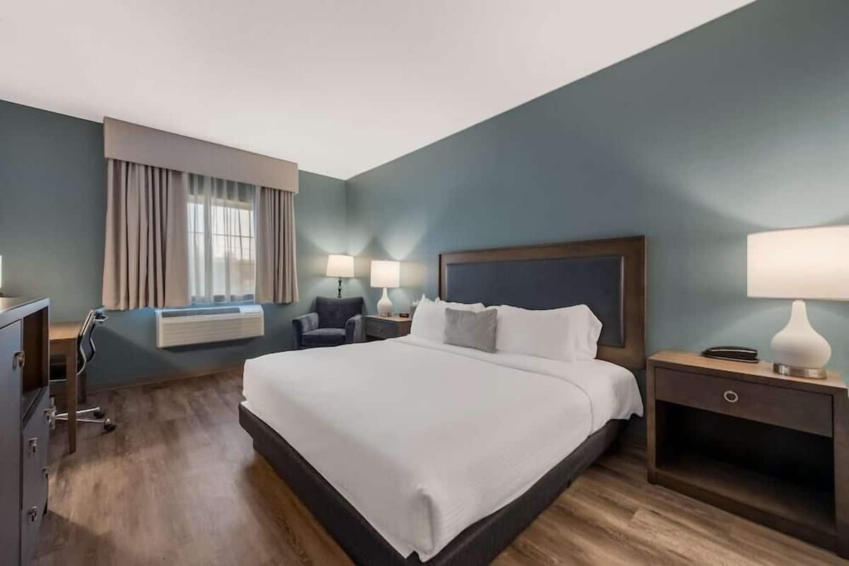 A hotel room with a large bed, bedside tables, a desk, a chair, and a window with curtains.