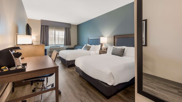 Habitación de hotel con dos camas, un escritorio, una silla, una lámpara y una ventana con cortinas.