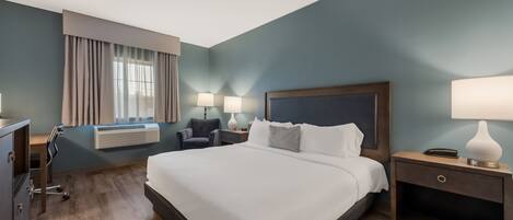 Una habitación de hotel con una cama grande, un escritorio, una silla, una mesita de noche y una lámpara.