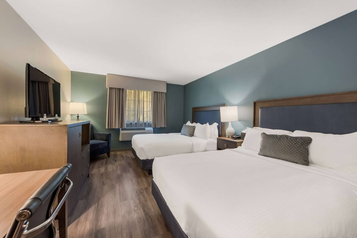 A hotel room with two beds, a desk, a TV, and a window with curtains.