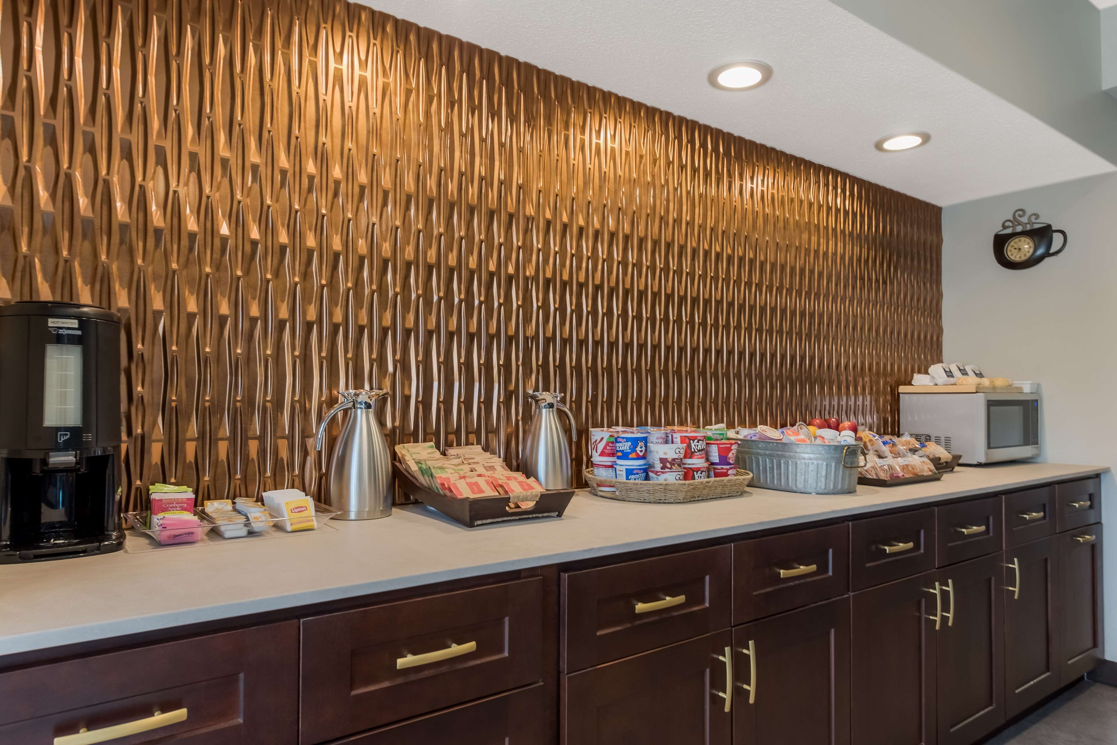 Zona de buffet con pared de madera, cafetera, hervidores y diferentes alimentos.
