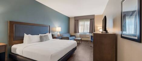 A hotel room with a large bed, a desk, a chair, a TV, and a window with curtains.