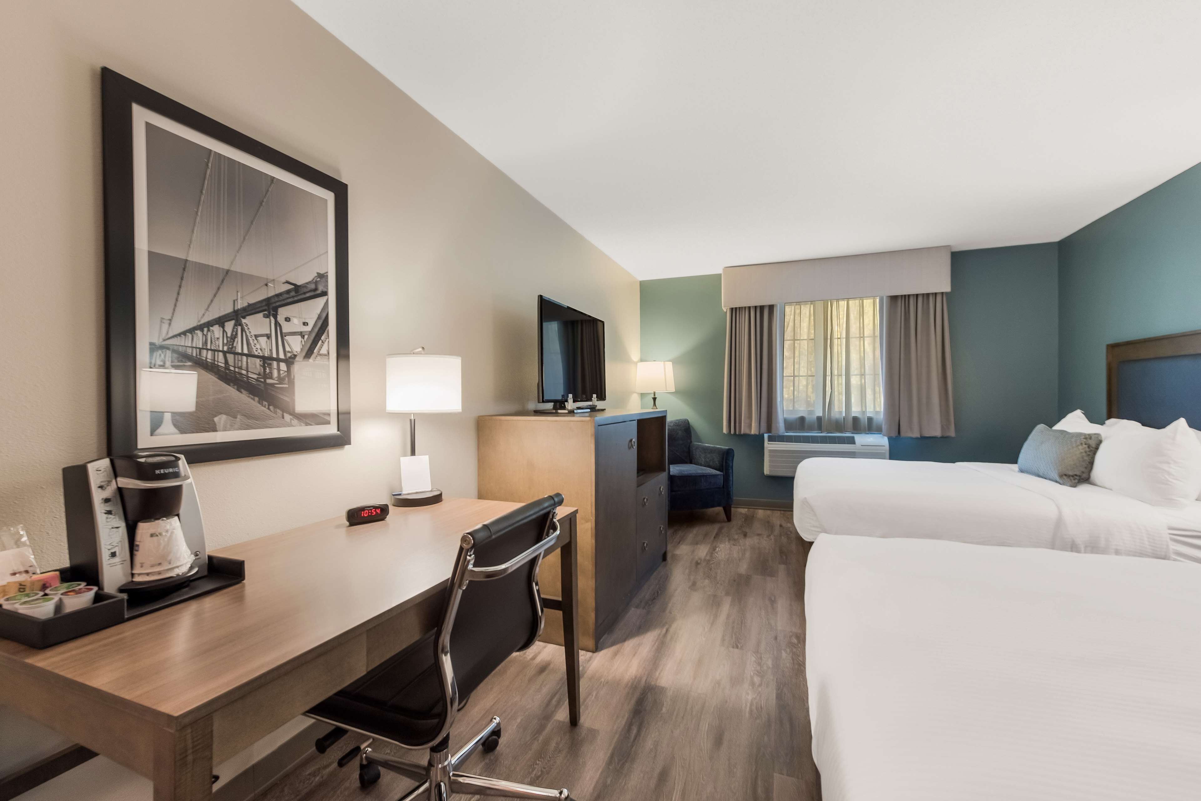 Habitación de hotel con escritorio, dos camas, un cuadro grande enmarcado, cafetera y televisor.