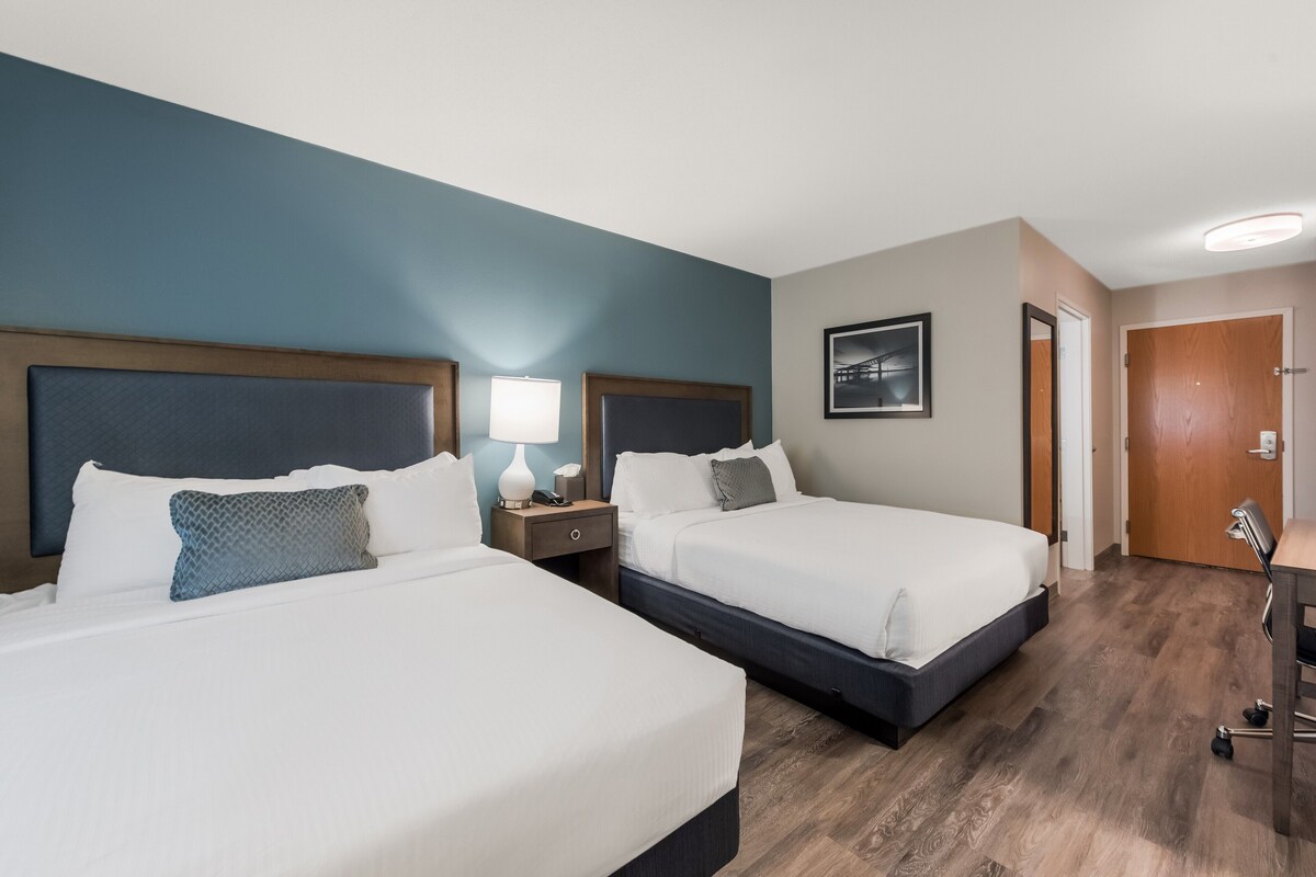A hotel room with two beds, a desk, and a door.