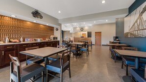 Un comedor moderno con mesas y sillas de madera, una encimera de cocina con electrodomésticos y un mural grande en la pared.