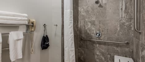 Uma área de chuveiro com barra de apoio, um porta-toalhas branco e um banquinho branco pequeno.
