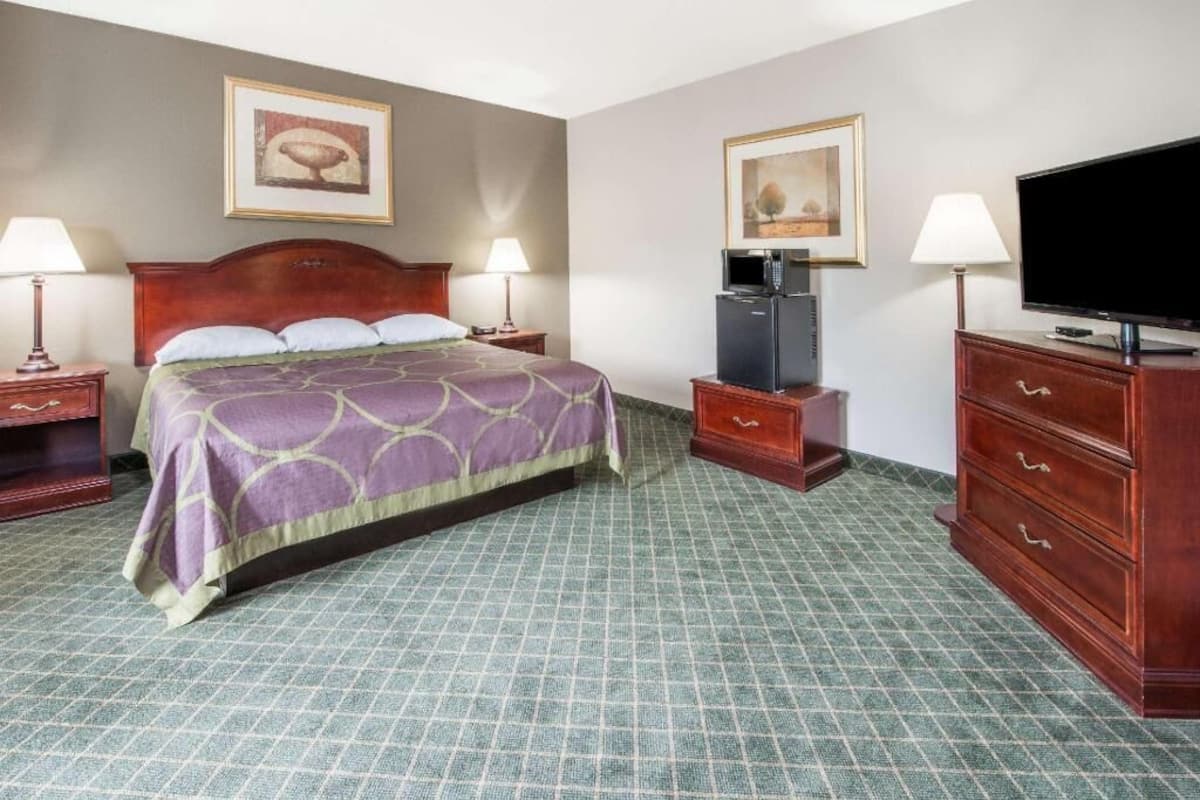 A hotel room with a bed, two bedside tables, a television, a dresser, and artwork on the walls.