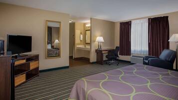 A hotel room with a large bed, a desk with a chair, a television, a bathroom with a sink and mirror, and a window with curtains.