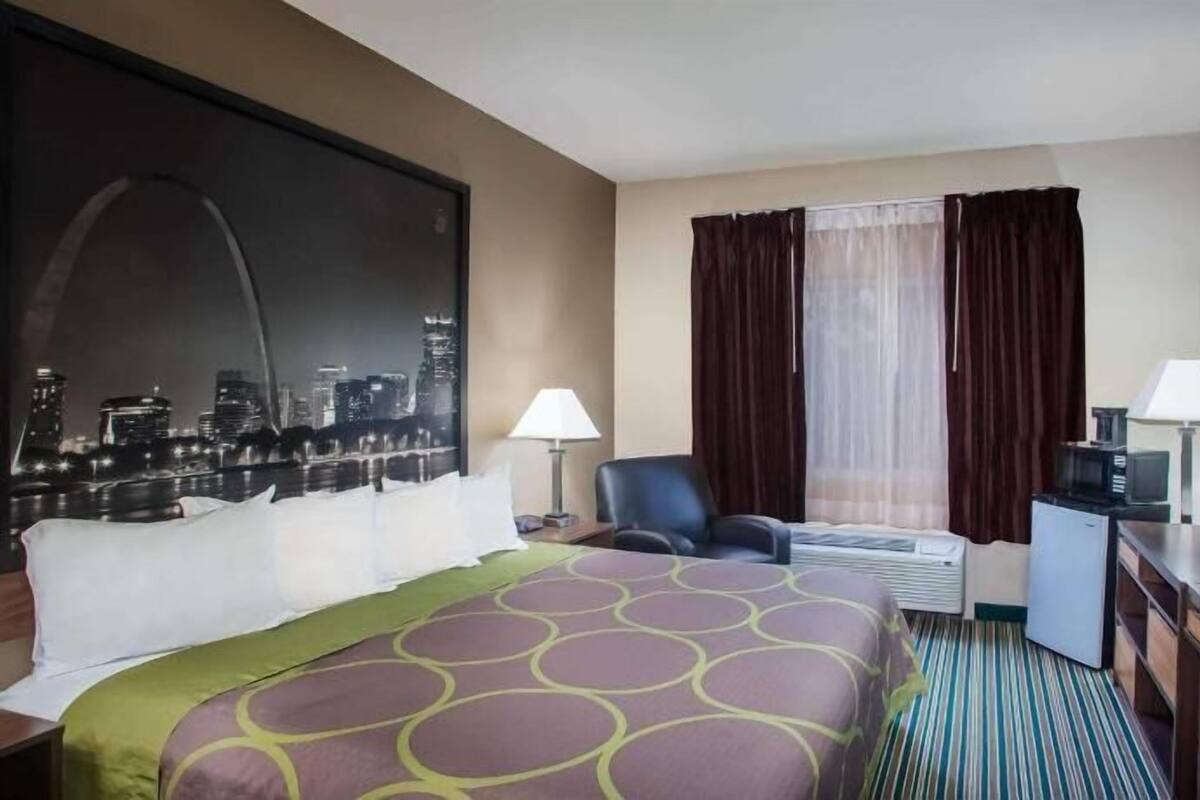 A hotel room with a bed, a chair, a television, a desk, and a window with curtains.