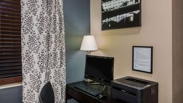 A hotel room with a desk, computer, printer, and a framed picture on the wall.