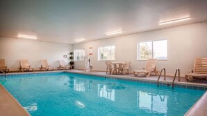 Une piscine intérieure à l’eau claire, entourée de chaises longues en bois et d’une table.