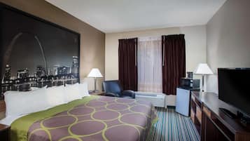 A hotel room with a large bed, two chairs, a desk with a TV, a mini-fridge, and a cityscape view.