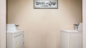 Une buanderie avec deux machines à laver blanches, une enseigne au-dessus indiquant « Wash and Dry Laundry Co. – laverie en libre-service », et un sol carrelé.