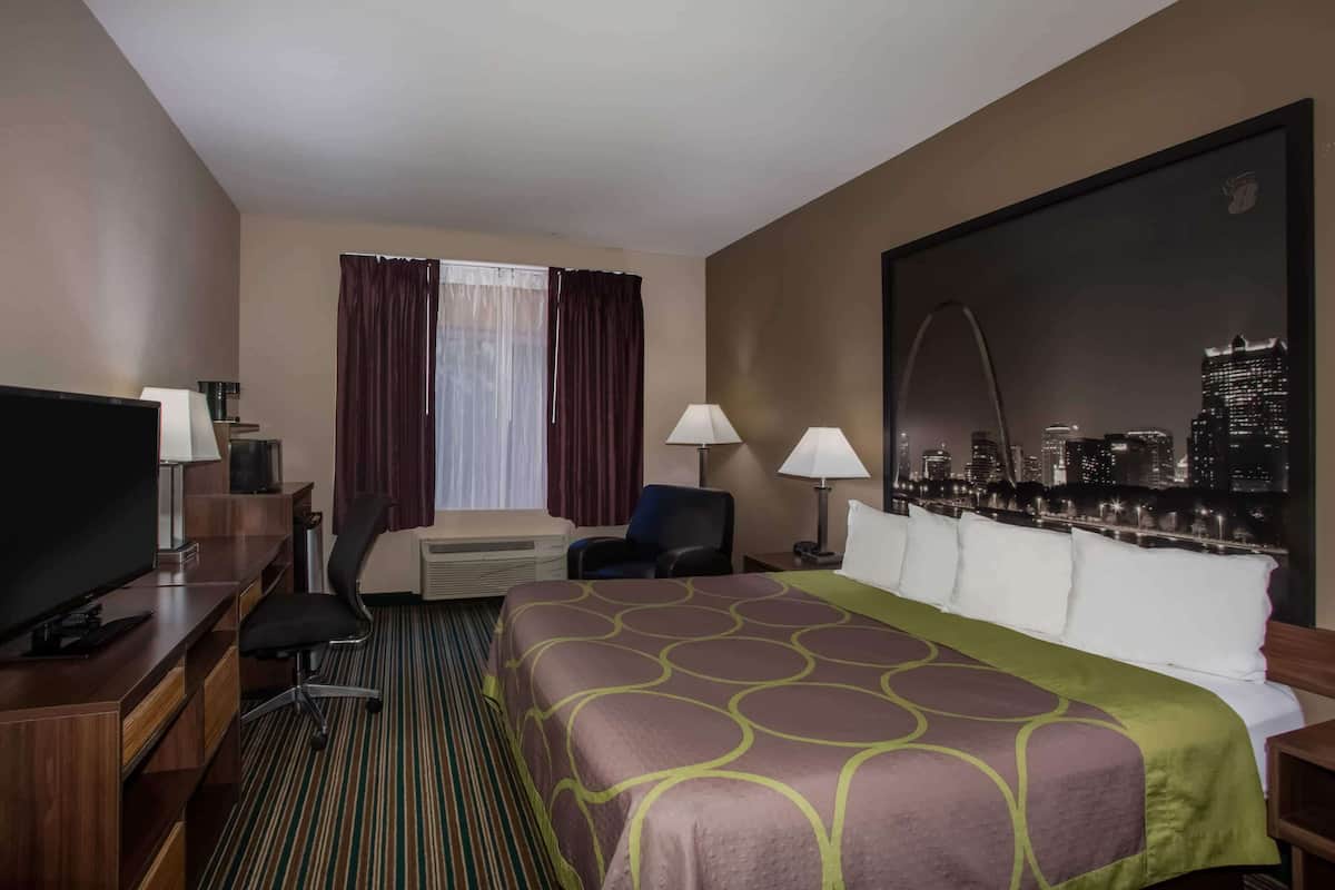 A hotel room with a bed, a desk with a TV, a chair, a window with curtains, and a cityscape view on the wall.