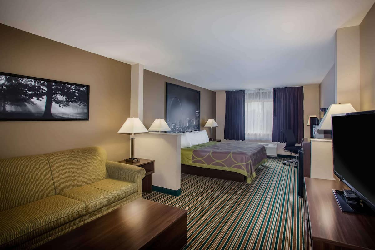 A hotel room with a sofa, a bed, a desk, a television, and two lamps.