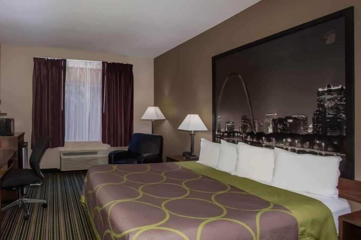 A hotel room with a bed, a desk with a TV, a chair, a window with curtains, a lamp, and a cityscape view.