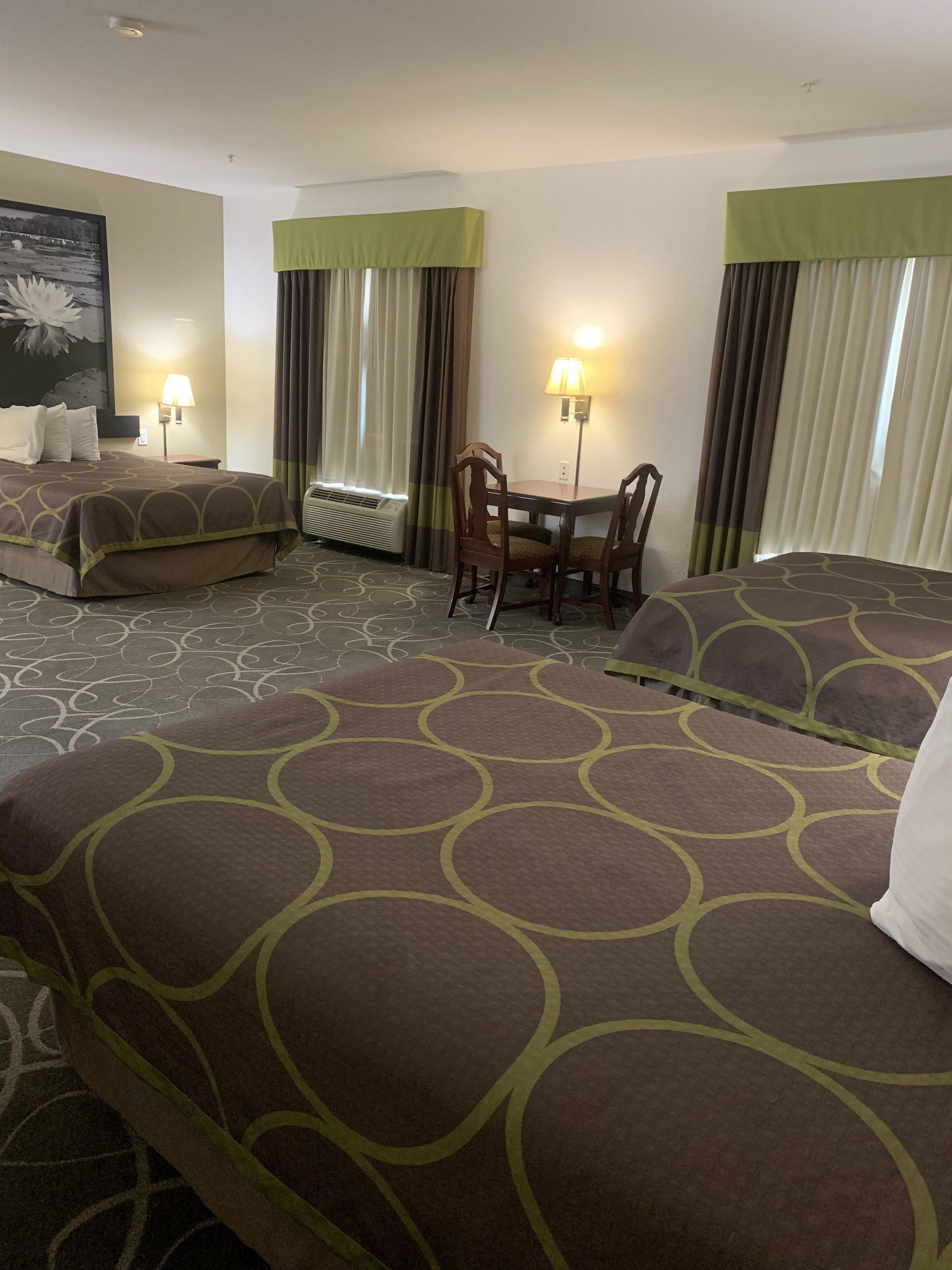 A hotel room with two beds, a dining table with chairs, a lamp, and a painting on the wall.