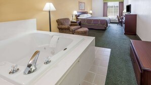 A hotel room with a large white bathtub, a bed with a green headboard, a desk with a computer, and a chair.