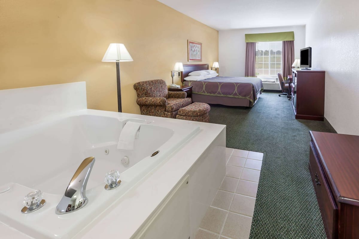 A hotel room with a large white bathtub, a bed with a green headboard, a desk with a computer, and a chair.