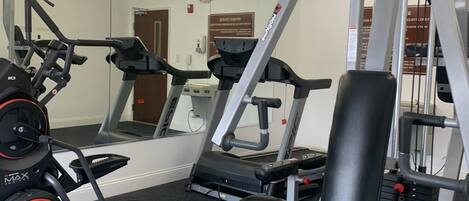 Une salle de sport équipée de matériel d’exercice, notamment un tapis de course, un banc de musculation et divers appareils.