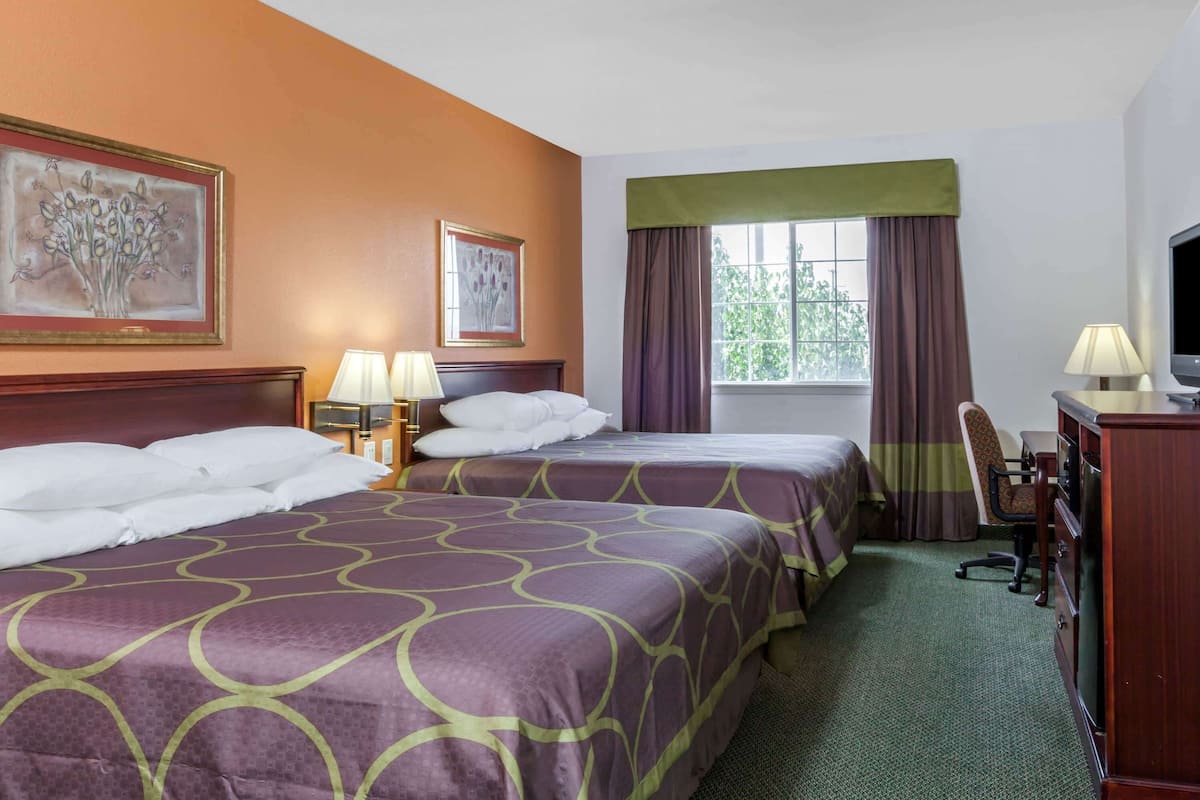 A hotel room with two beds, a desk, a chair, a television, and artwork on the walls.