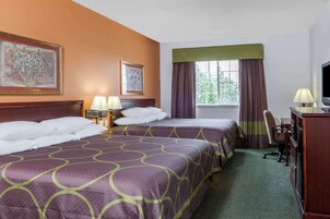 Habitación de hotel con dos camas, un escritorio, una silla, un televisor y obras de arte en las paredes.