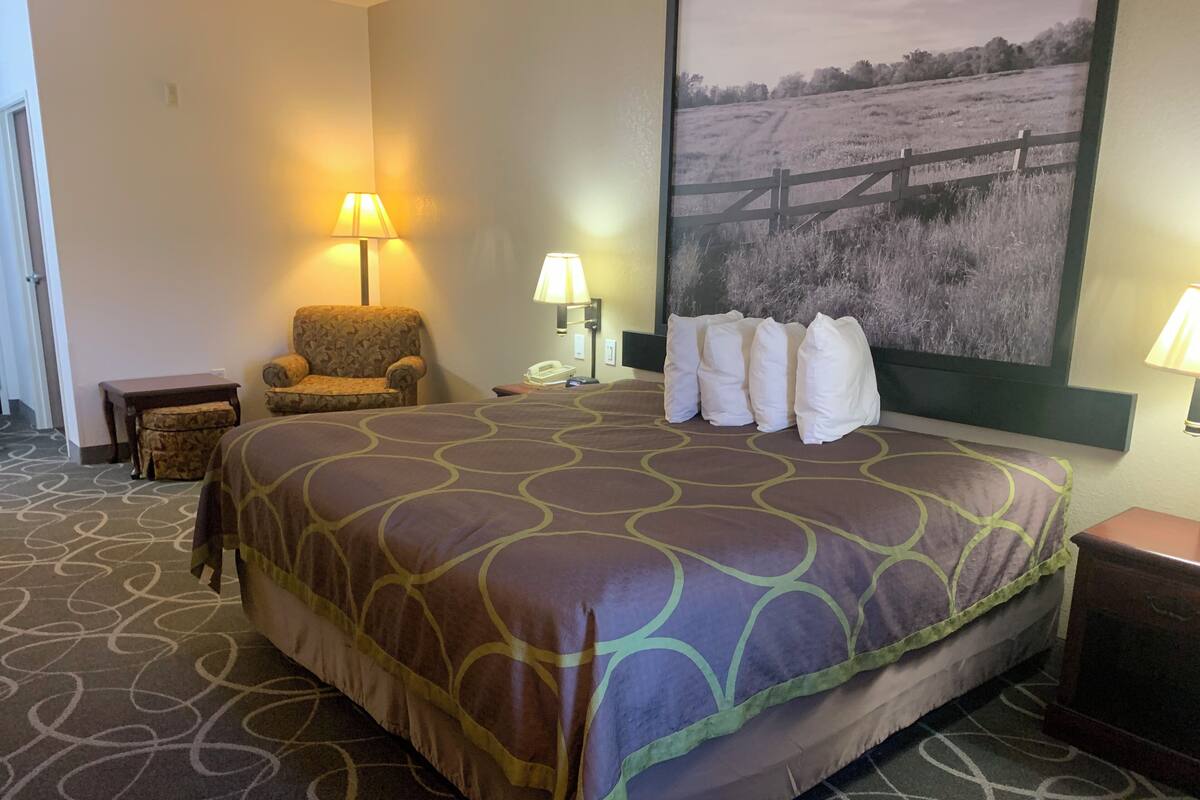 A hotel room with a large bed, two chairs, a small table, and a wall-mounted TV.