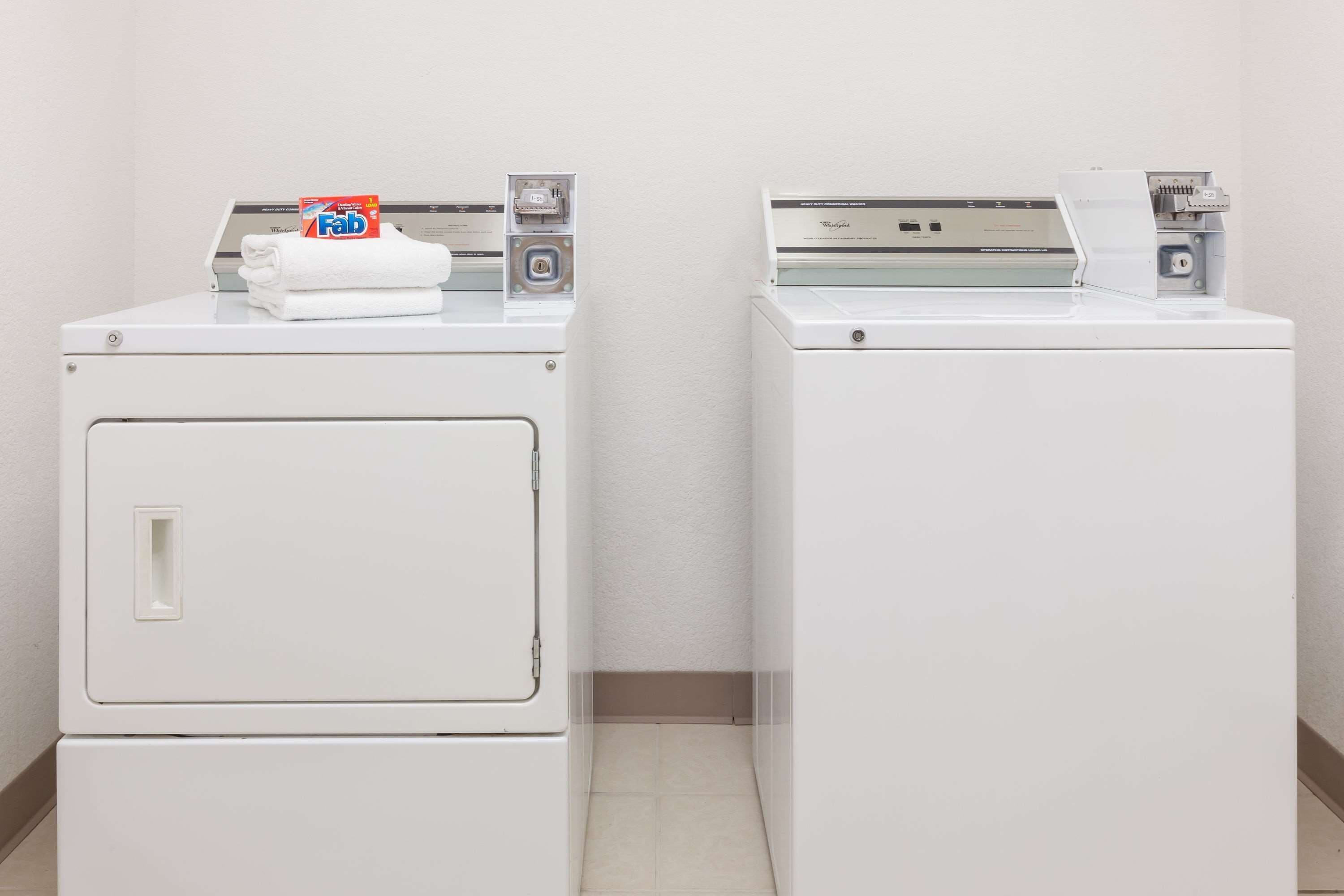Two white front-loading washing machines in a laundry room with a plain wall and tiled floor.