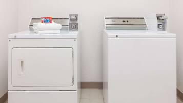 Two white front-loading washing machines in a laundry room with a plain wall and tiled floor.