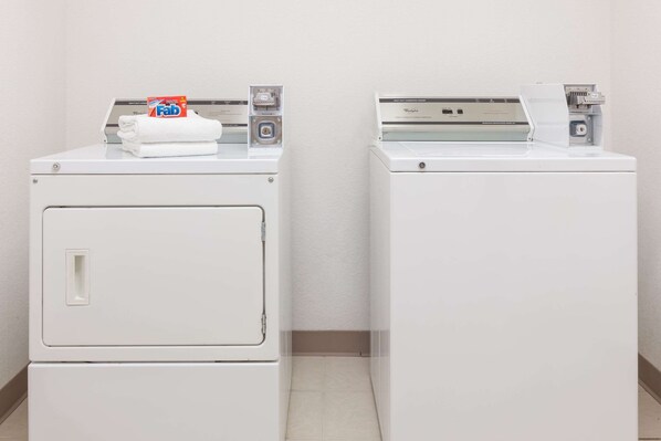 Two white front-loading washing machines in a laundry room with a plain wall and tiled floor.