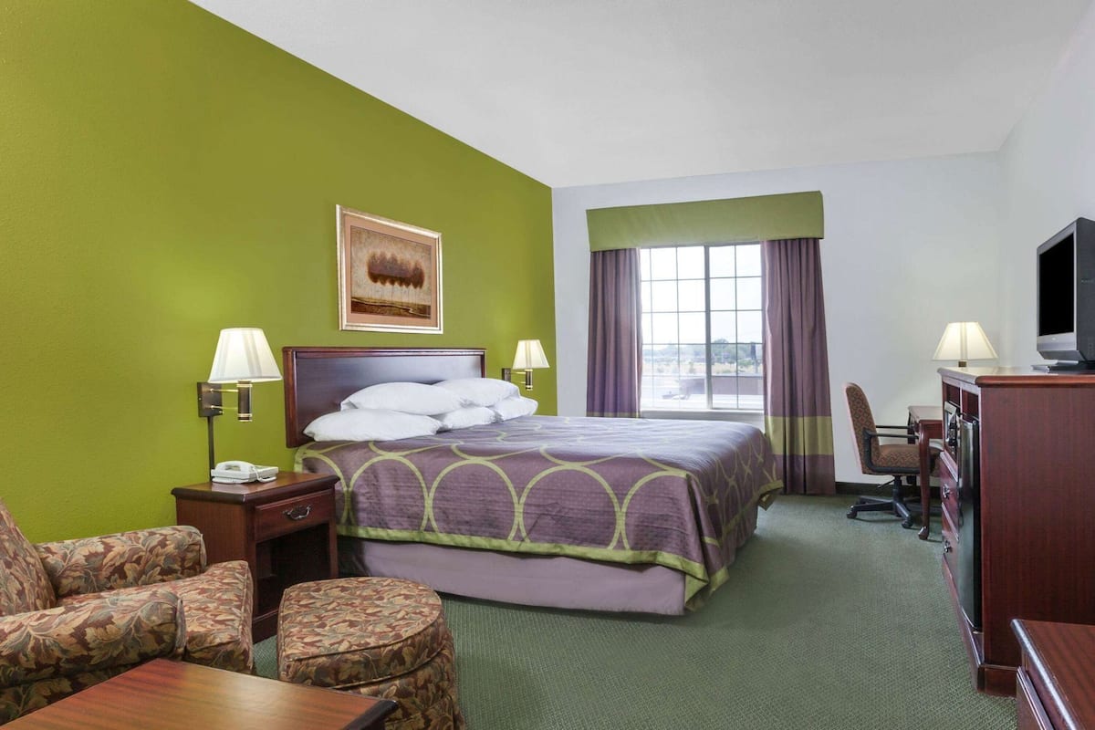 A hotel room with a bed, a desk, a chair, a TV, and a painting on the wall.