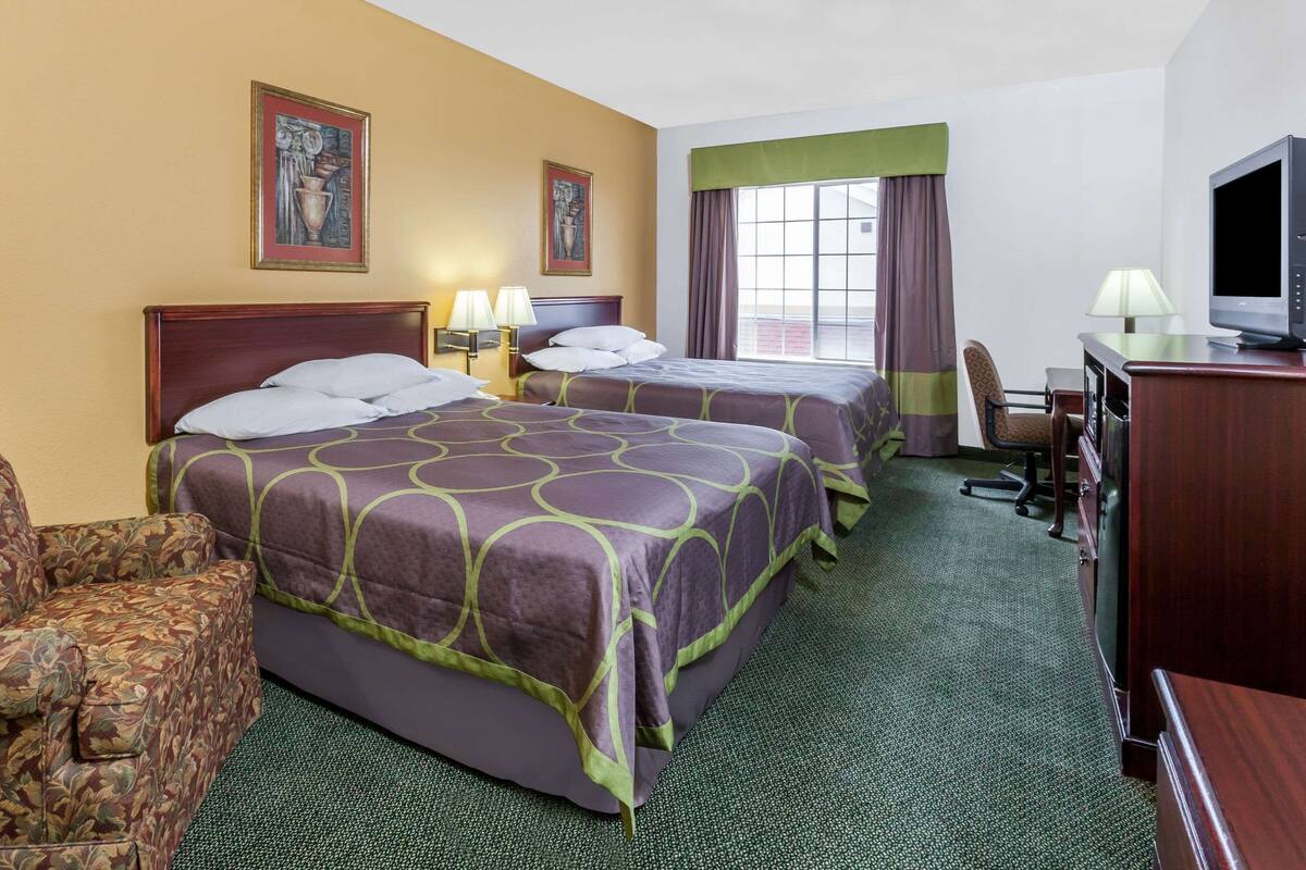 A hotel room with two beds, a desk, a chair, and a television.
