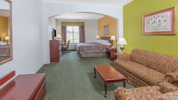 Habitación de hotel con cama, sofá, escritorio y silla. Hay una ventana con cortinas, un cuadro en la pared y una lámpara en el escritorio.