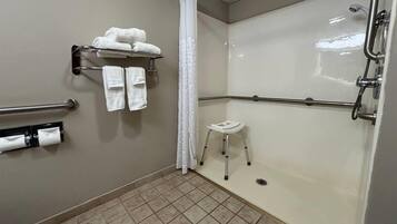 Un baño con ducha, barras de apoyo, toallero y un taburete.