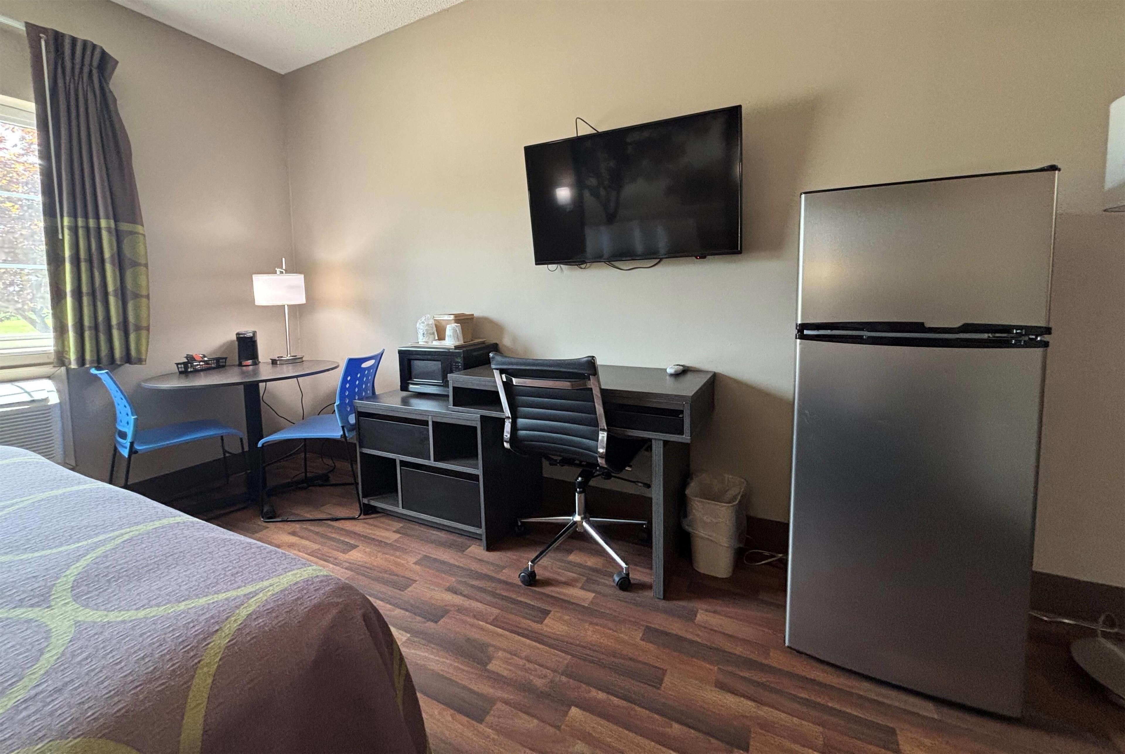Een hotelkamer met een bed, bureau, stoel, televisie en koelkast.