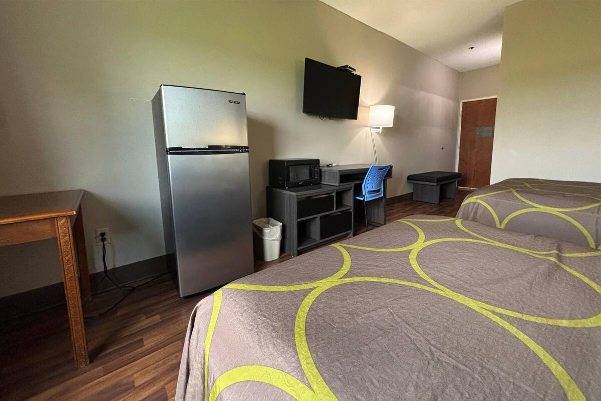A hotel room with a bed, a desk with a computer, a refrigerator, a microwave, a TV, and a trash can.