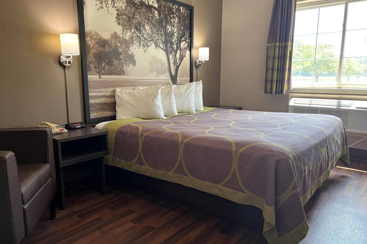 A neatly made bed with a patterned bedspread, two bedside lamps, a nightstand with a phone, and a large framed picture on the wall.